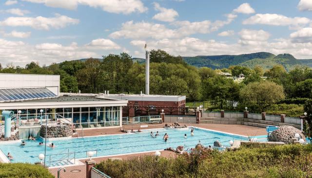 Aussenbecken mit Hallenbad, im Hintergrund eine grüne Hügelkette